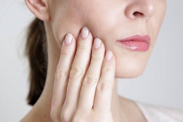 Woman touching the side of her jaw, indicating discomfort often associated with TMJ disorder
