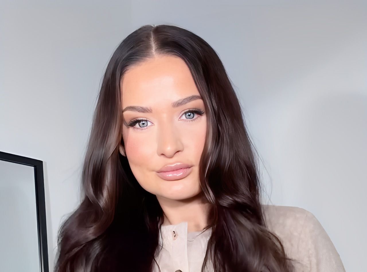 Front-facing portrait of Emily Lucy with long dark hair, wearing a neutral-toned outfit indoors